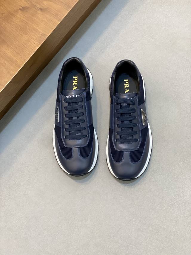prada 普拉达 男士新款牛皮拼接运动鞋 这款运动鞋呈现现代版型，以利落线条与流畅细节重新演绎品牌典藏款型。鞋履采用小牛皮革和科技织物打造，外侧饰有三角金属徽