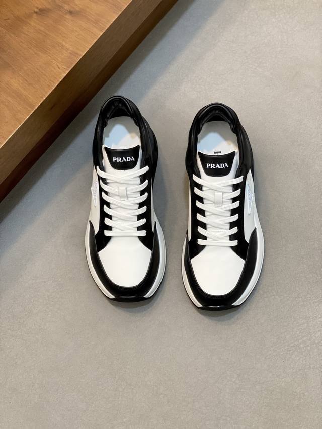 prada 普拉达 男士新款皮面拼接运动鞋 这款运动鞋呈现现代版型，以利落线条与流畅细节重新演绎品牌典藏款型。鞋履采用小牛皮革和科技织物打造，外侧饰有三角金属徽